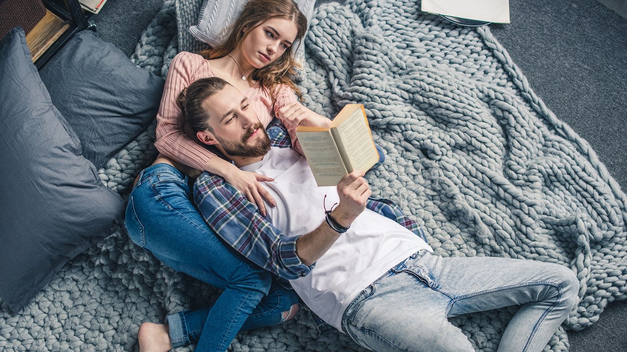 Beautiful young couple lying on knitted blanket and reading book
