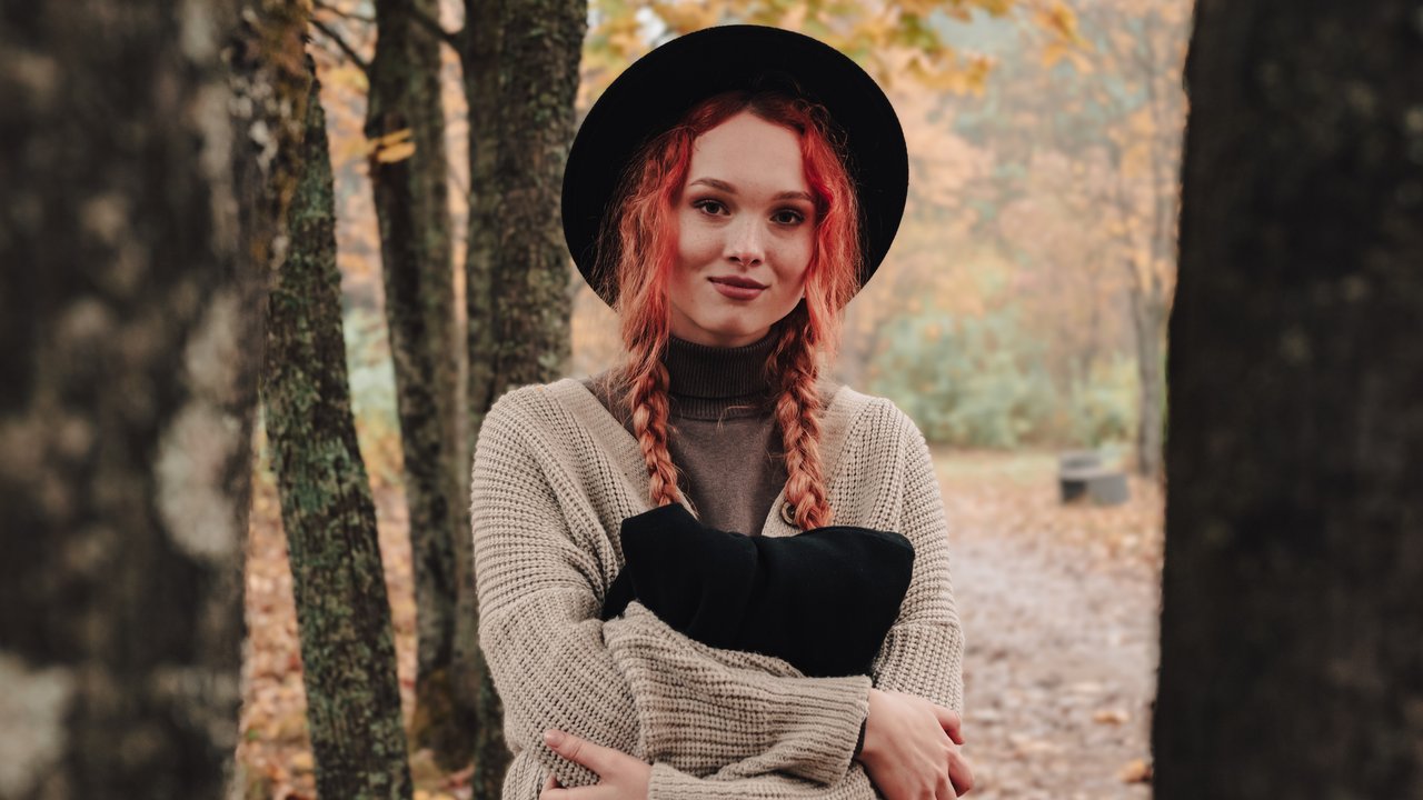 Fashionable women's autumn portrait in the park area. Red haired girl in a glasses, black hat with pigtails in stands against the background of withering foliage. Fashionable women's autumn portrait in the park area. Red haired girl in a glasses, black hat with pigtails in stands against the background of withering foliage.