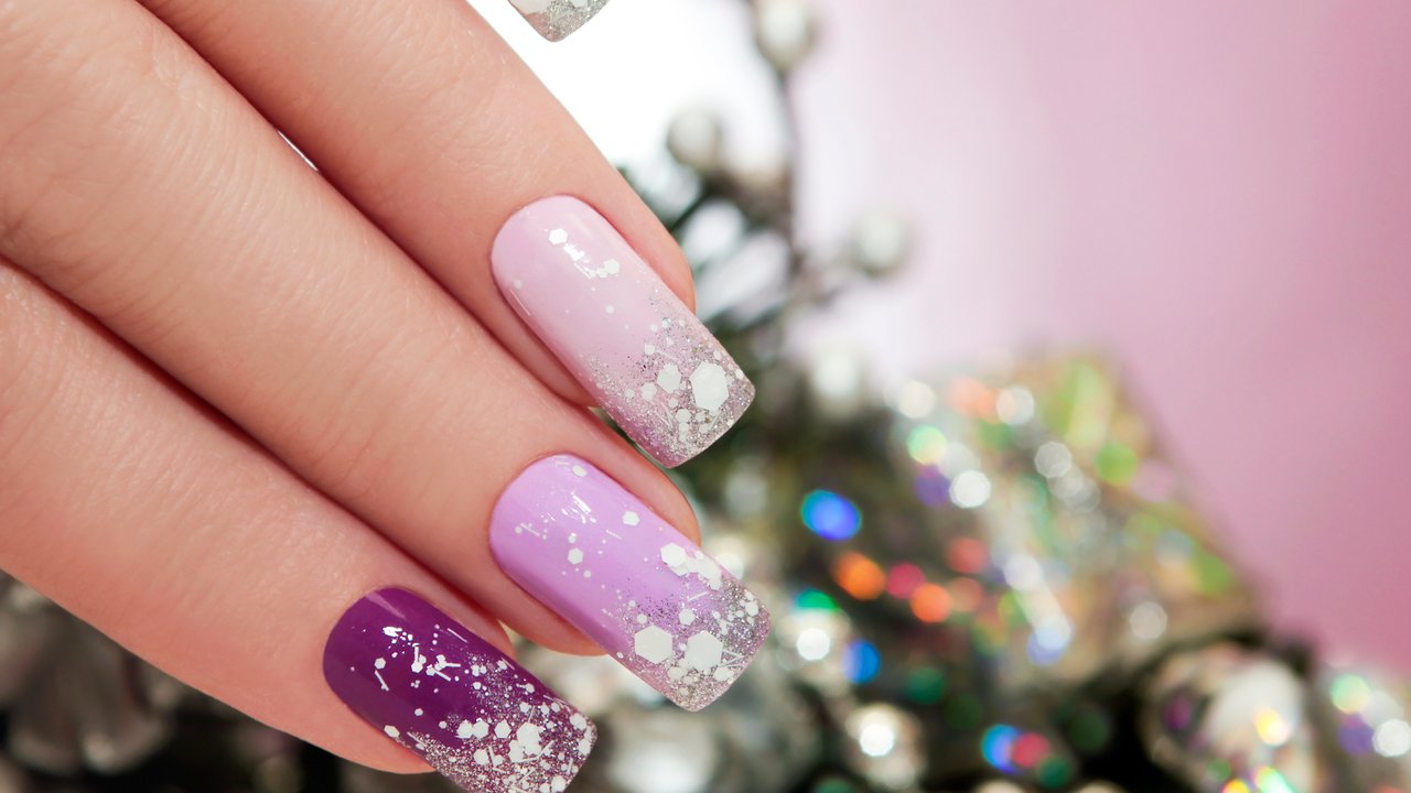 Lilac nail Polish with sparkles and snowflakes on the background of Christmas tree decorations.