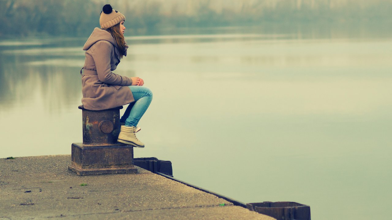 Lonely teenage girl sitting on the dock on cold winter day.