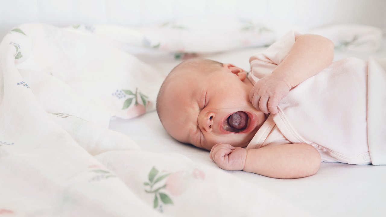 Newborn baby girl sleeps and yawning. Child's first days of life at home.