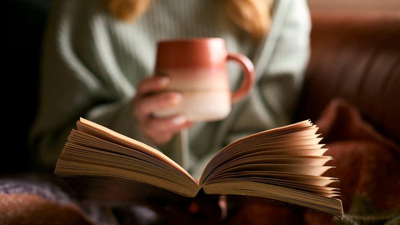 Eine Frau hält in der einen Hand ein aufgeschlagenes Buch und in der anderen eine Tasse Eine Frau hält in der einen Hand ein aufgeschlagenes Buch und in der anderen eine Tasse