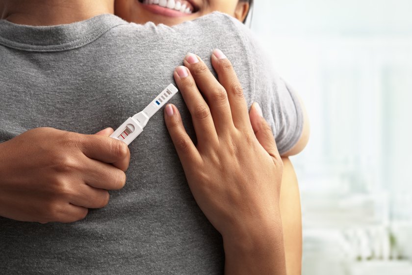 Paar umarmt sich, Frau hält einen Schwangerschaftstest in der Hand