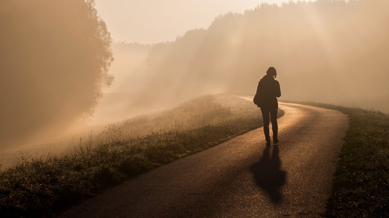 Eine Frau geht an einem nebeligen Morgen allein auf einer Landstraße Eine Frau geht an einem nebeligen Morgen allein auf einer Landstraße