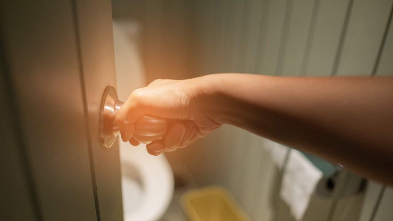 Eine Frauenhand öffnet die Badezimmertür zur Toilette Eine Frauenhand öffnet die Badezimmertür zur Toilette