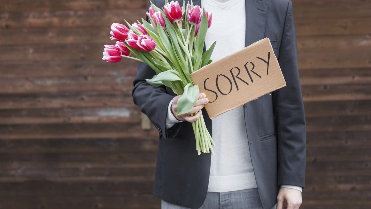 Mann entschuldigt sich mit Blumen und Sorry-Schild