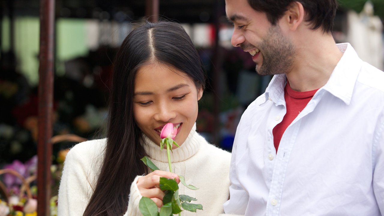 Close up portrait of a beautiful young woman smelling rose with boyfriend smiling