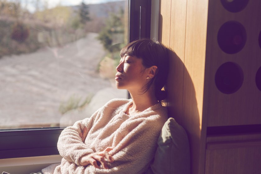 Frau mit geschlossenen Augen sitzt an einem Fenster Frau mit geschlossenen Augen sitzt an einem Fenster