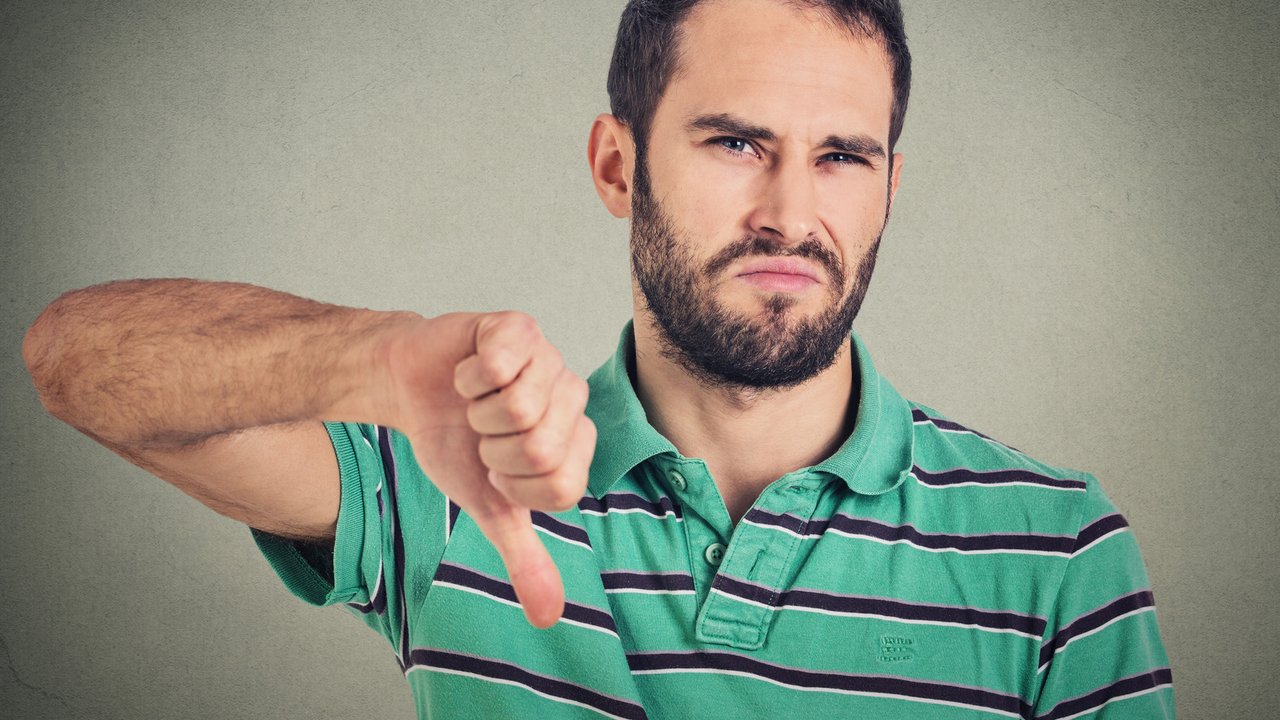 Closeup portrait angry, unhappy, young man showing thumbs down sign, in disapproval of offer situation isolated on gray background. Negative human emotions, facial feelings