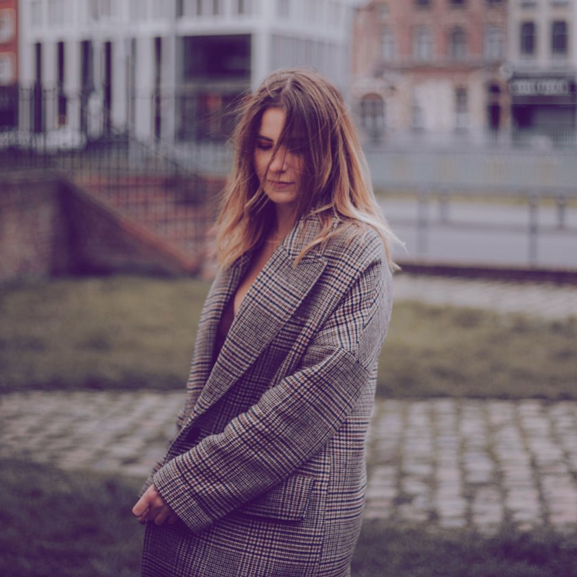Frau in kariertem Mantel mit gesenktem Blick Frau in kariertem Mantel mit gesenktem Blick