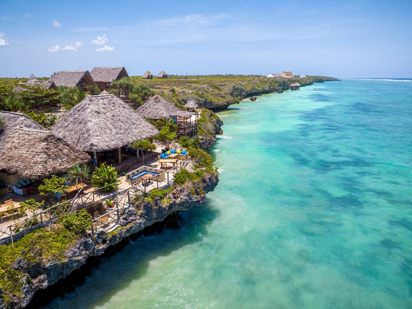 Breathtaking aerial view of a tropical paradise showcasing thatched roof houses perched on a cliff edge, offering stunning views of the crystal-clear ocean in Michamvi, Zanzibar Breathtaking aerial view of a tropical paradise showcasing thatched roof houses perched on a cliff edge, offering stunning views of the crystal-clear ocean in Michamvi, Zanzibar