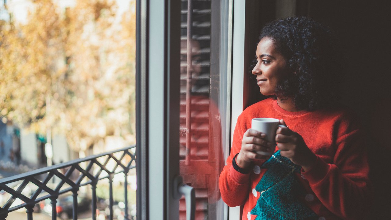 Smiling woman at home drinking coffee and enjoying the city view
