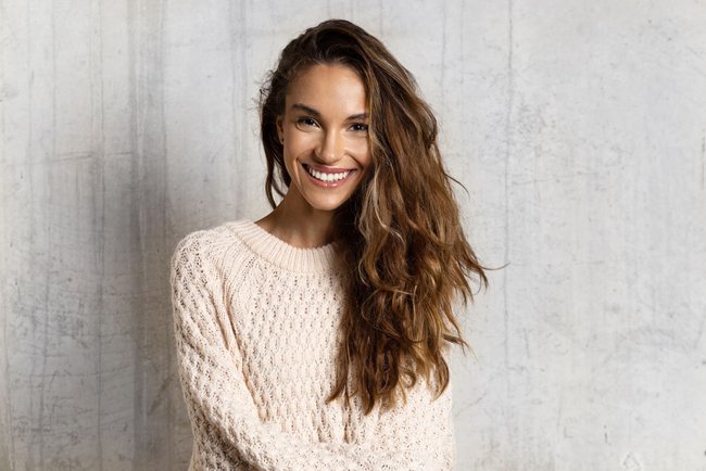 Portrait of cheerful smiling girl. Lovely girl with healthy dark hair posing isolated on beige background in warm sweater. Beauty and winter concept Portrait of cheerful smiling girl. Lovely girl with healthy dark hair posing isolated on beige background in warm sweater. Beauty and winter concept