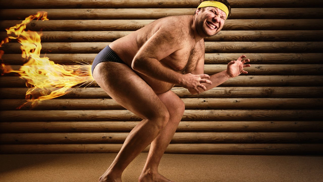 Very strange naked man farts by fire on the background of wooden wall