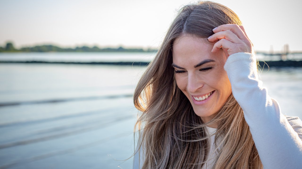 portrait of a beautiful young Women on a beach with sunlight and water in background laughing ans looking down with hand in her hair portrait of a beautiful young Women on a beach with sunlight and water in background laughing ans looking down with hand in her hair