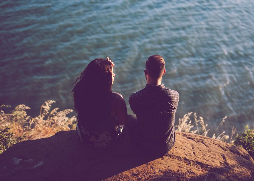 Mann und Frau, die am Hang sitzen und aufs Wasser schauen Mann und Frau, die am Hang sitzen und aufs Wasser schauen