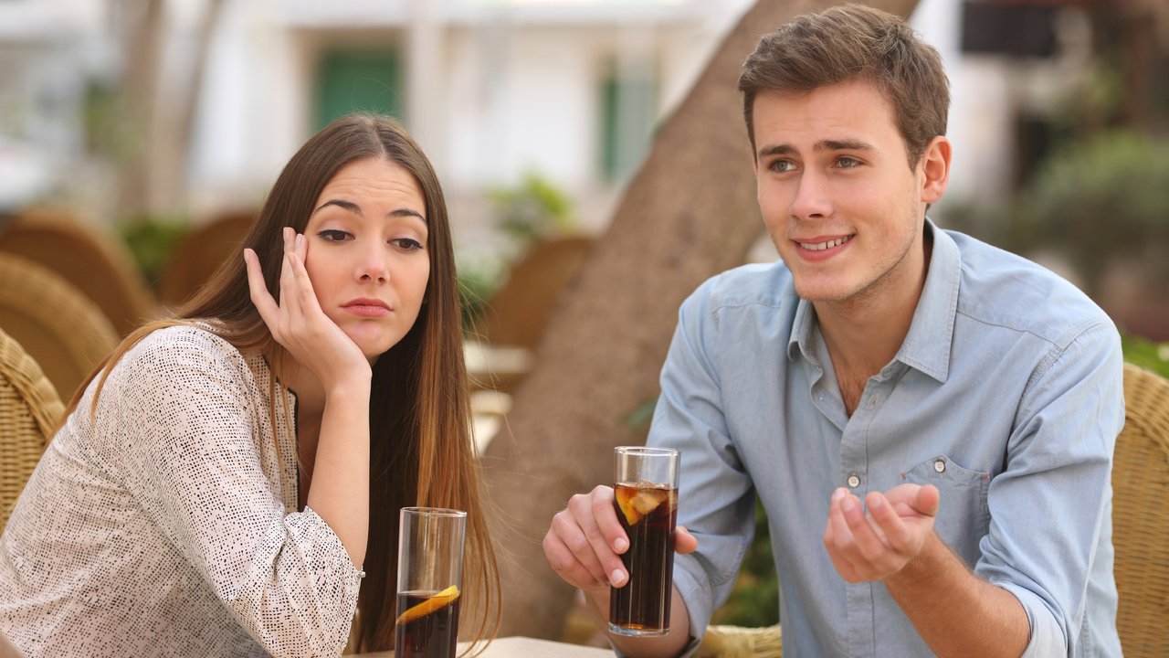 Man and woman dating in a restaurant terrace but she is boring while he speaks