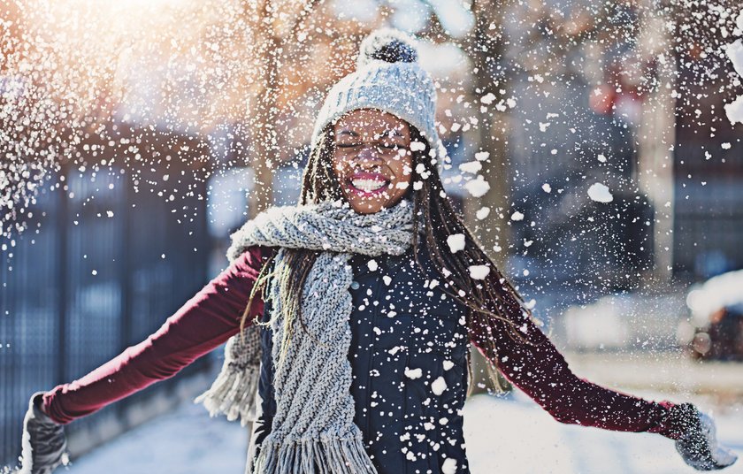 Eine junge Frau spielt mit Schnee, der auf sie schneit und lacht dabei Eine junge Frau spielt mit Schnee, der auf sie schneit und lacht dabei