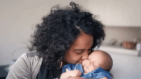 Frau wiegt Baby im Arm und küsst es auf die Wange
