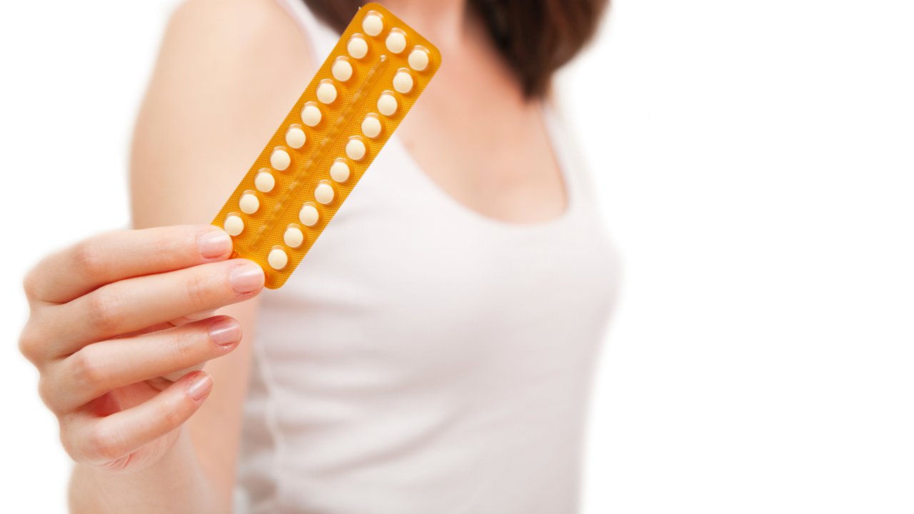Portrait of a young woman holding birth control pills