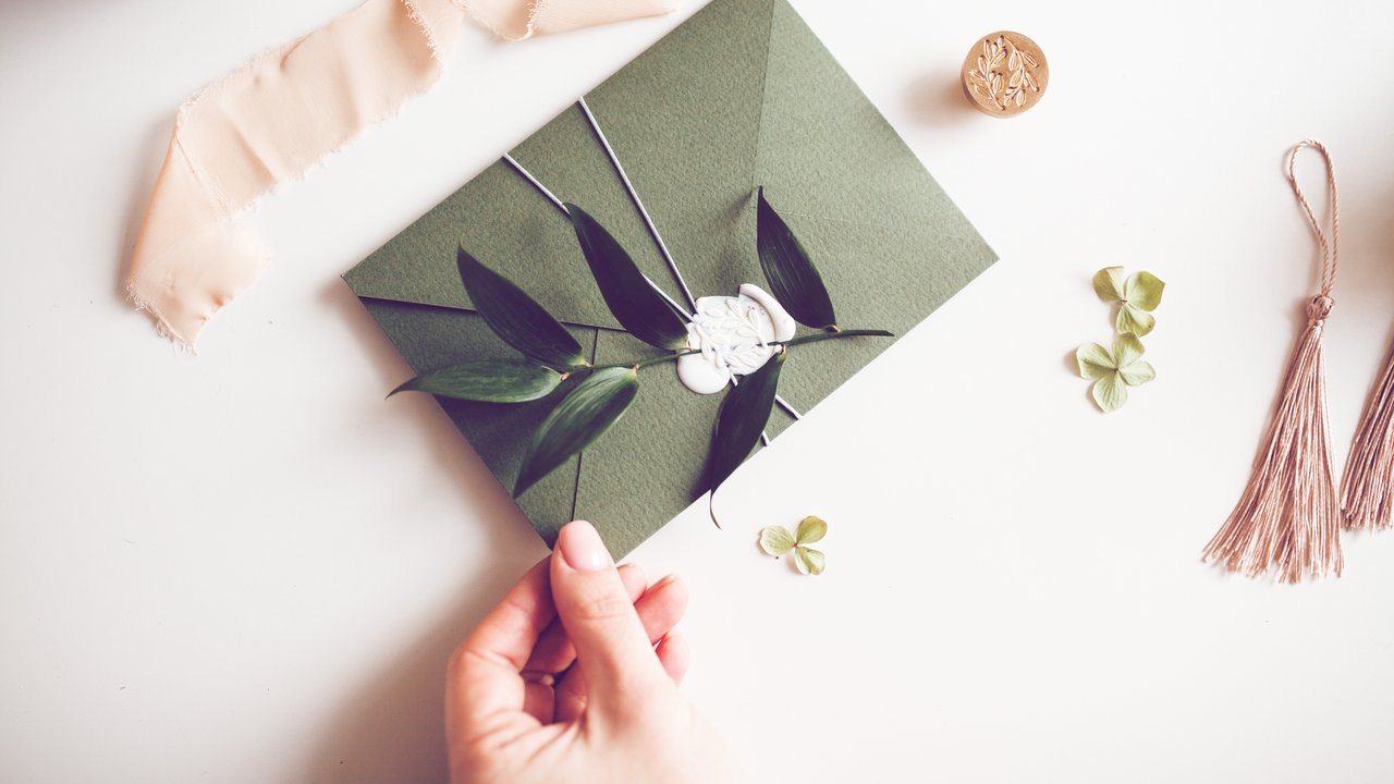 Green envelope with white wax seal stamp, green plant branch and peach ribbon on white background