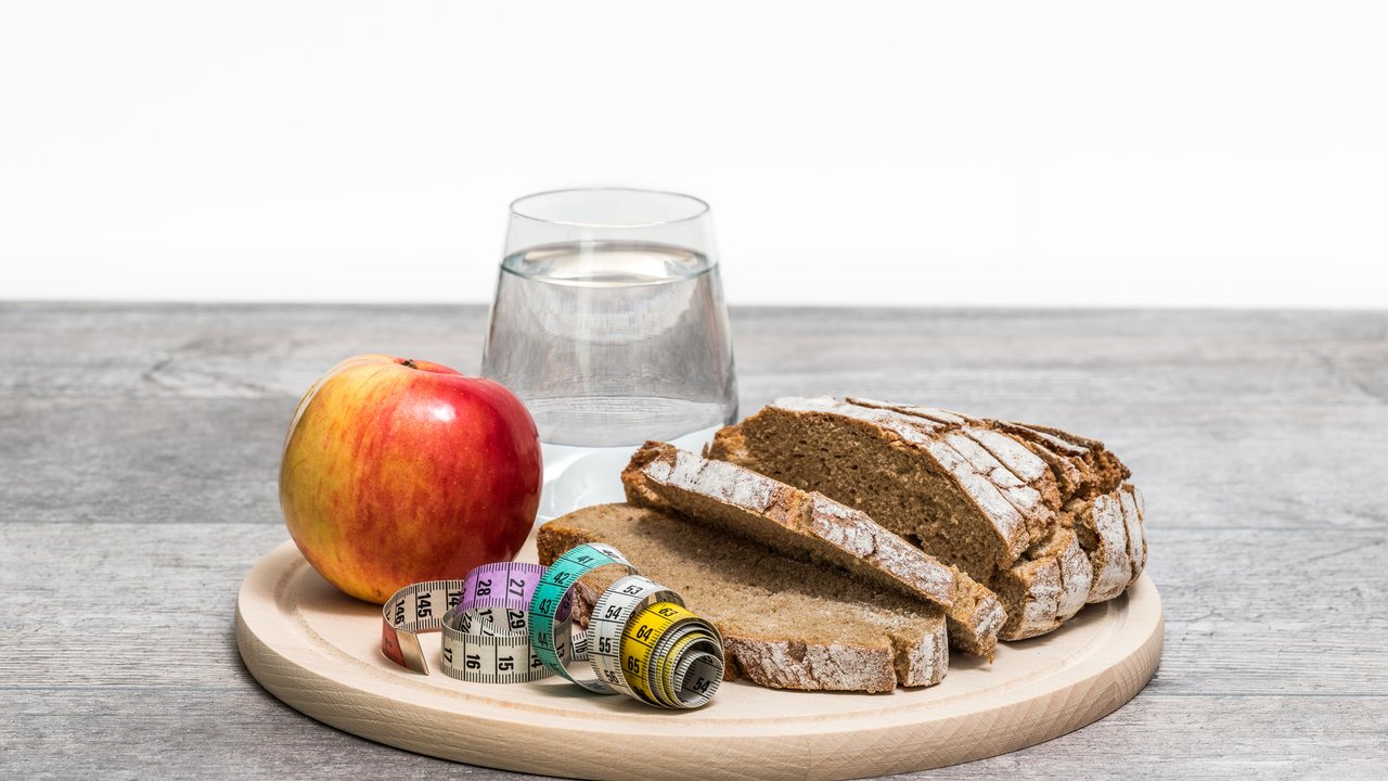 Healthy diet meal with apple, bread, tape measure and water on a round plate on a wooden floor with white background.