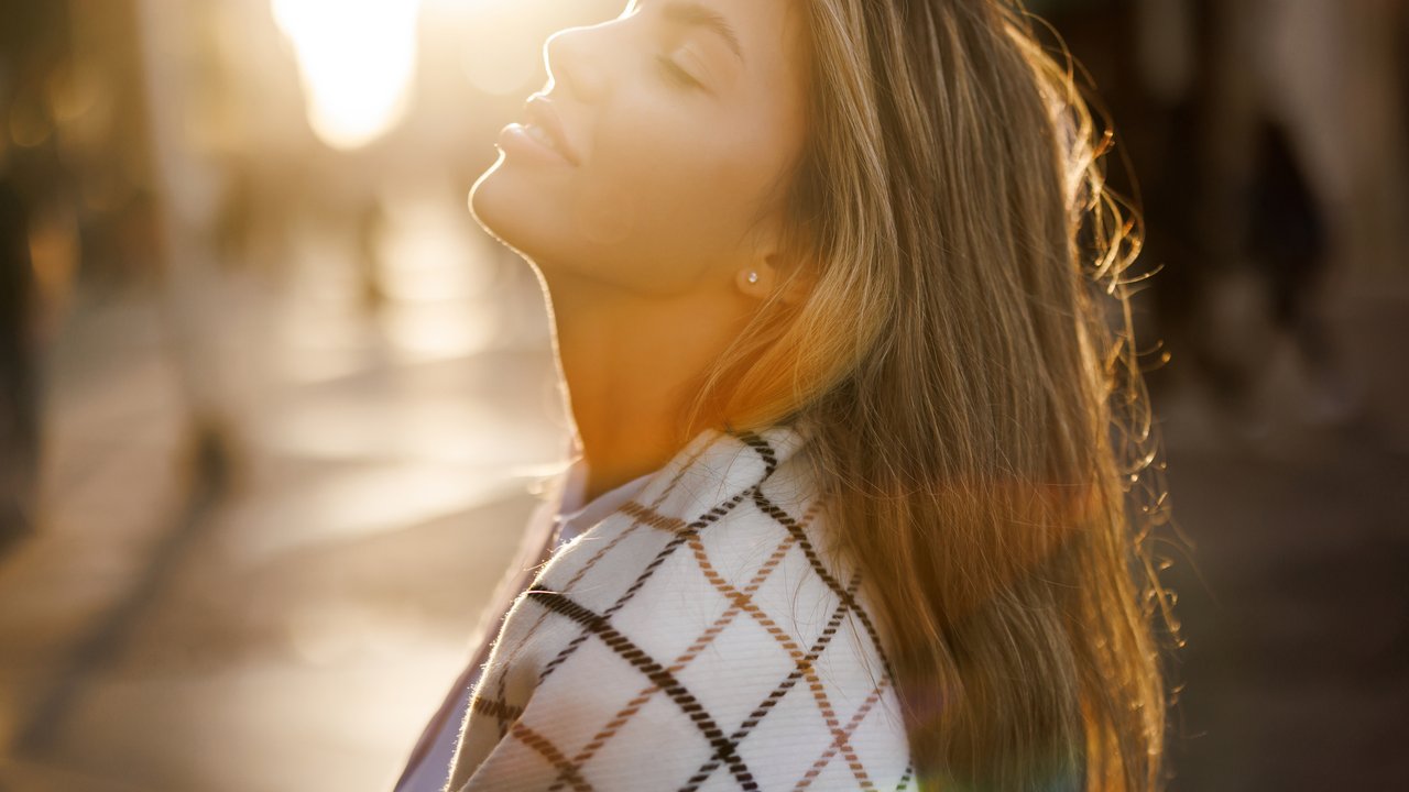 Eine Nahaufnahme einer Frau, die herbstliche Sonnenstrahlen genießt und die Augen geschlossen hat Eine Nahaufnahme einer Frau, die herbstliche Sonnenstrahlen genießt und die Augen geschlossen hat