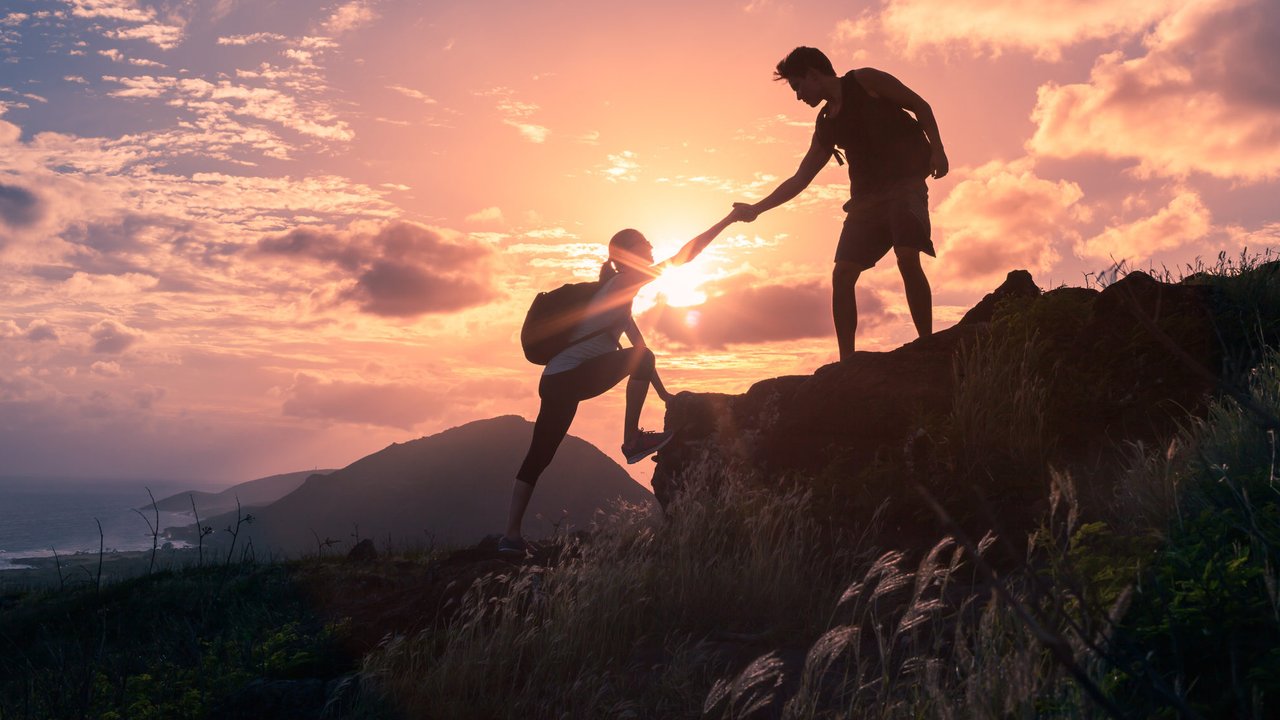 Male and female hikers climbing up mountain cliff and one of them giving helping hand.