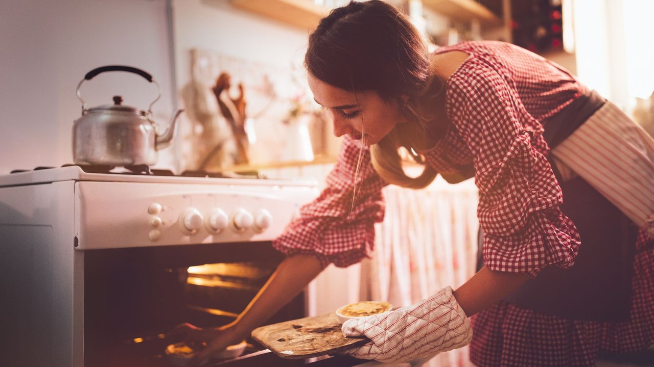 Eine junge Frau in der Küche ist dabei, Küchlein aus dem Ofen zu holen Eine junge Frau in der Küche ist dabei, Küchlein aus dem Ofen zu holen
