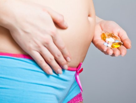 Schwangere Frau hält Tabletten vor dem Bauch
