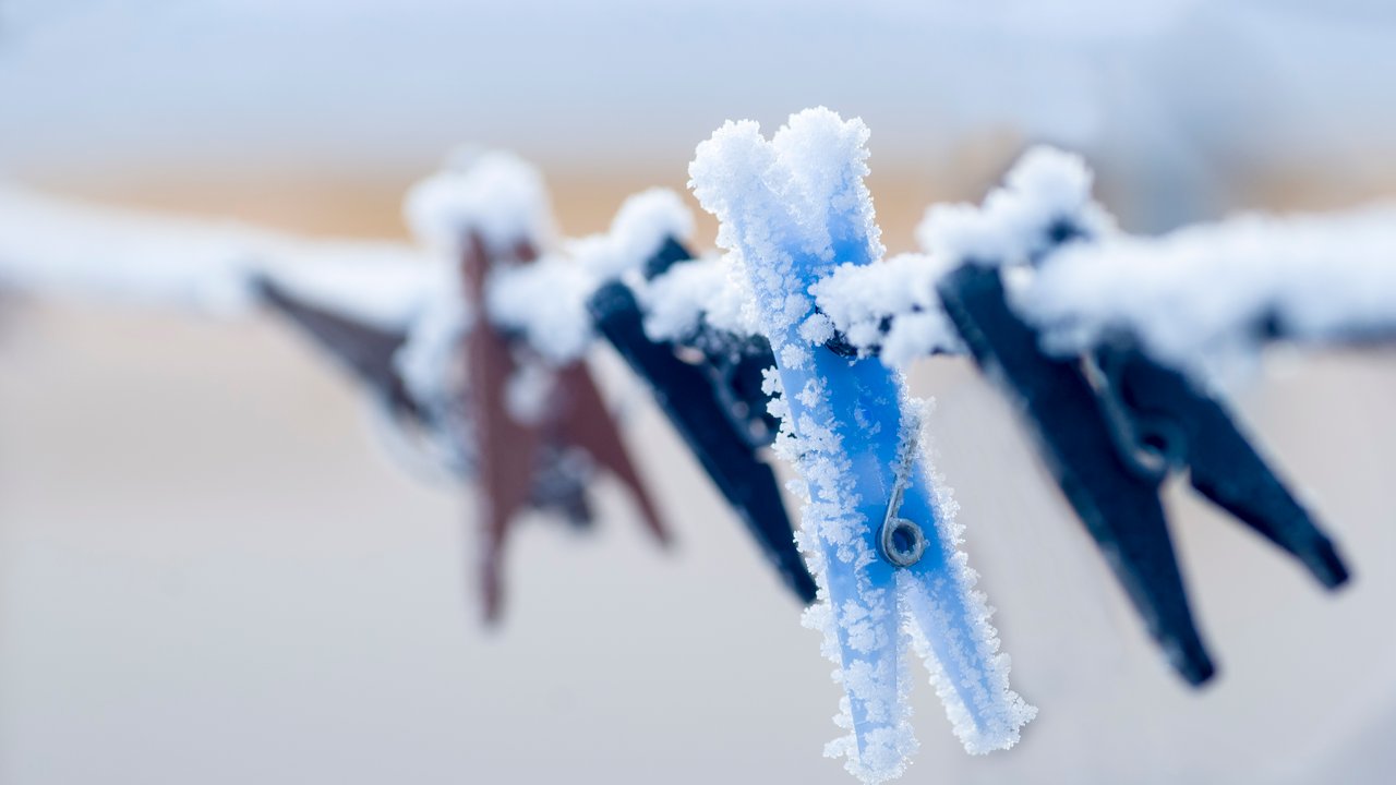 Frozen colorful clothes-pins on a rope at winter morning