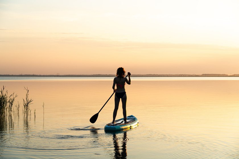 Sports girl on board for glanders surfing. A young slender woman floats on a board with a paddle. Surfing. Summer fun on the water. Healthy lifestyle. Woman stand up paddle boarding SUP on calm water
