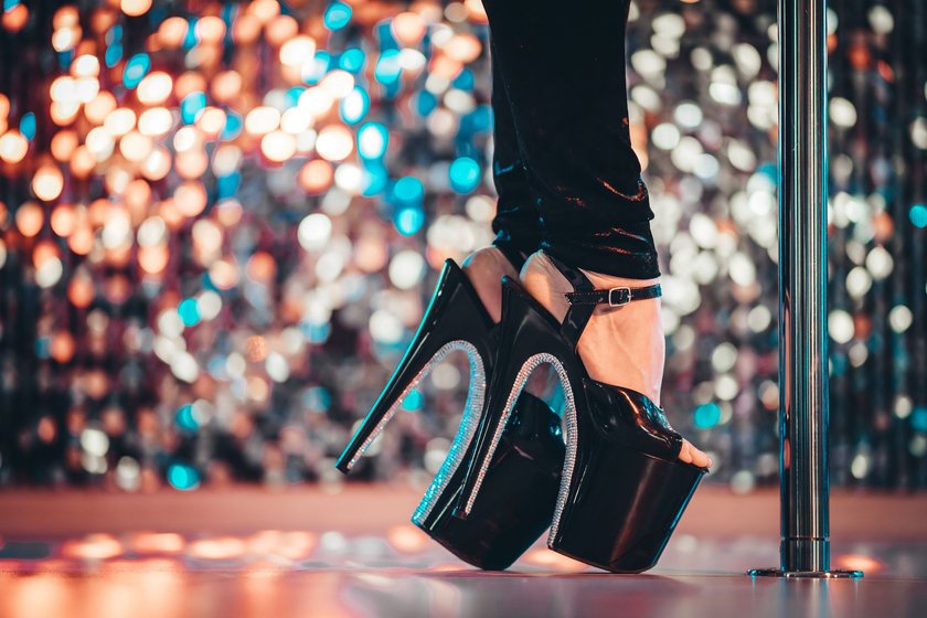 Legs in high sexy shoes near pylone. Striptease dancer moving on stage in strip night club. Pole dancing background