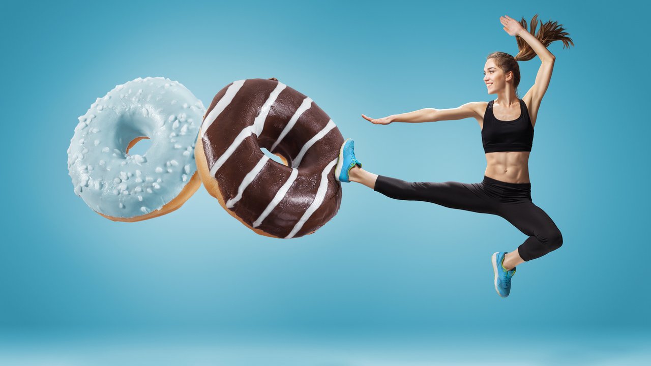 Fit young woman fighting off bad food on a  blue background. Concept of diet and healthy lifestile
