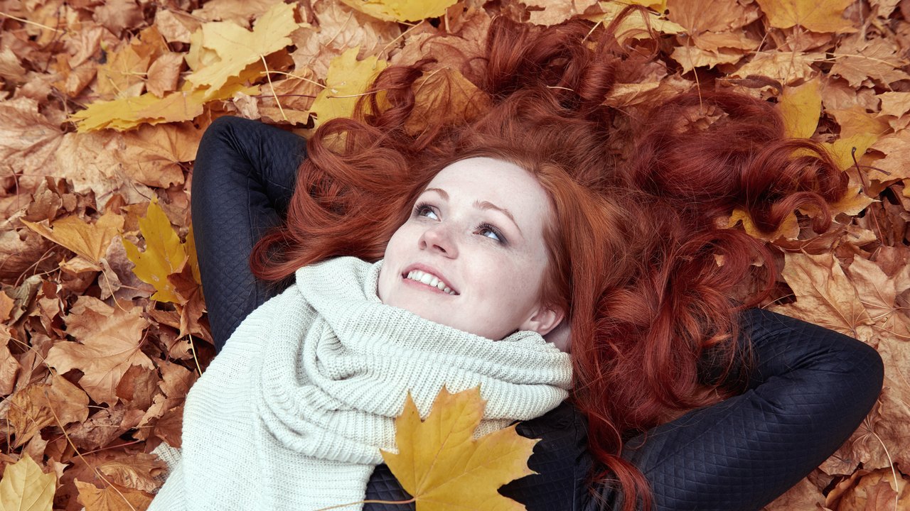 redhead girl lying on leaves in city park, fall season