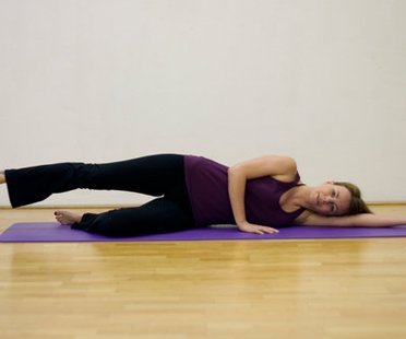 Schritt 1 der Pilatesübung Side Kicks, bei der die Pilateslehrerin auf dem Rücken liegt