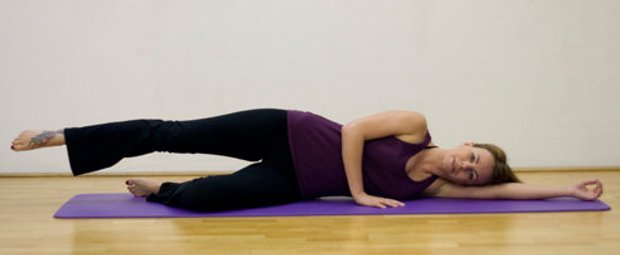 Schritt 1 der Pilatesübung Side Kicks, bei der die Pilateslehrerin auf dem Rücken liegt