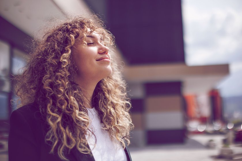 Frau mit Locken streckt ihr Gesicht in die Sonne
