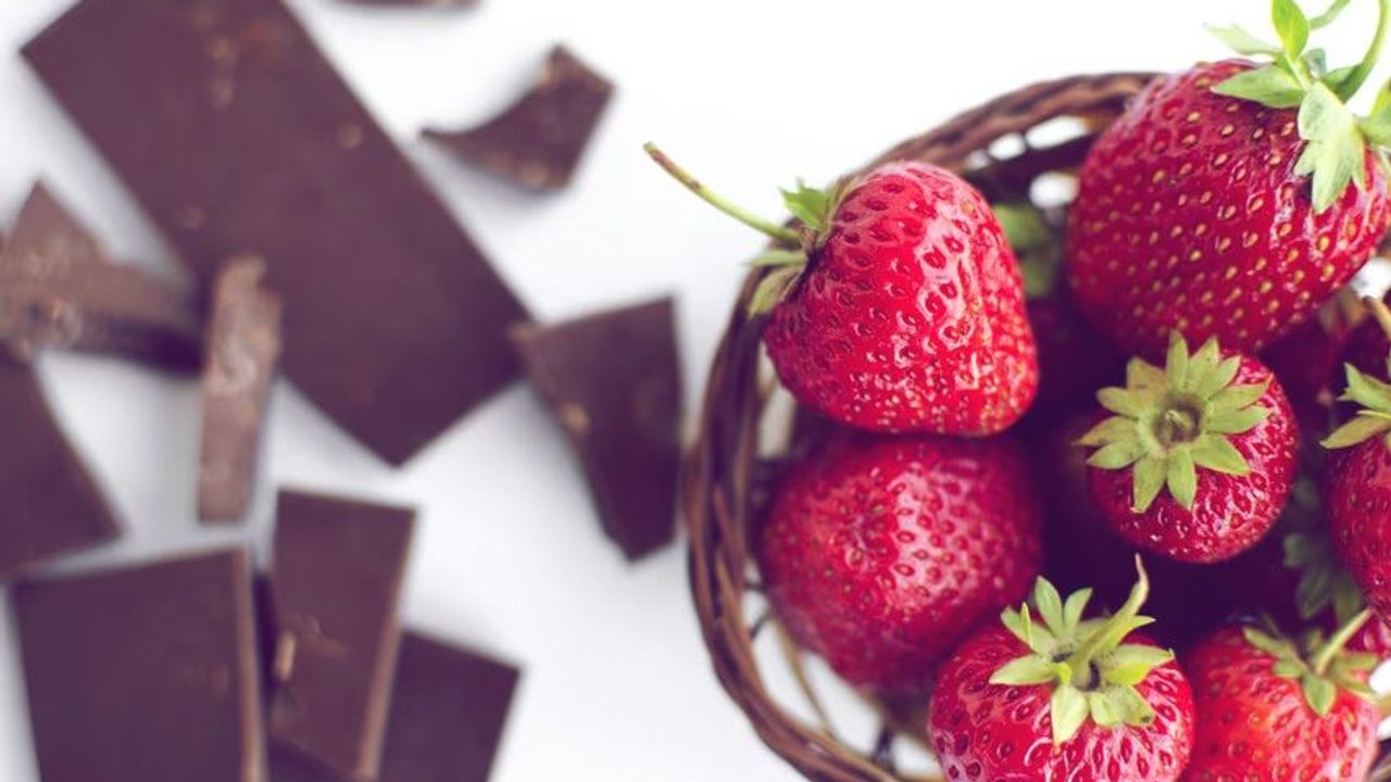 Broken chocolate, strawberries in a wicker basket on a white background