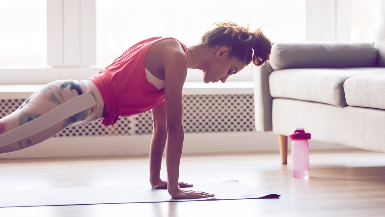 Young attractive sportive woman wearing activewear doing push ups or press ups exercise position on sport mat at home, practicing yoga plank pose, working out indoors, healthy active lifestyle concept
