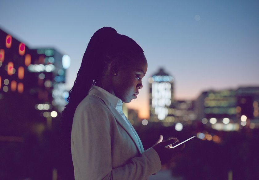 Frau schaut nachts auf ihr Smartphone, Skyline im Hintergrund