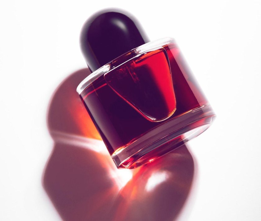 Red perfume bottle laying on a white background with a long shadow & light reflection