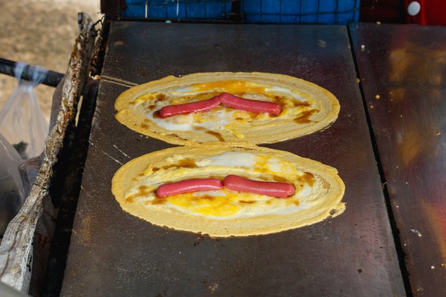 Khanom Tokyo wird dieser thailändische Straßen-Snack genannt. Die herzhafte Variante ist ein Hot Dog mit Ei im Pfannkuchenteig.