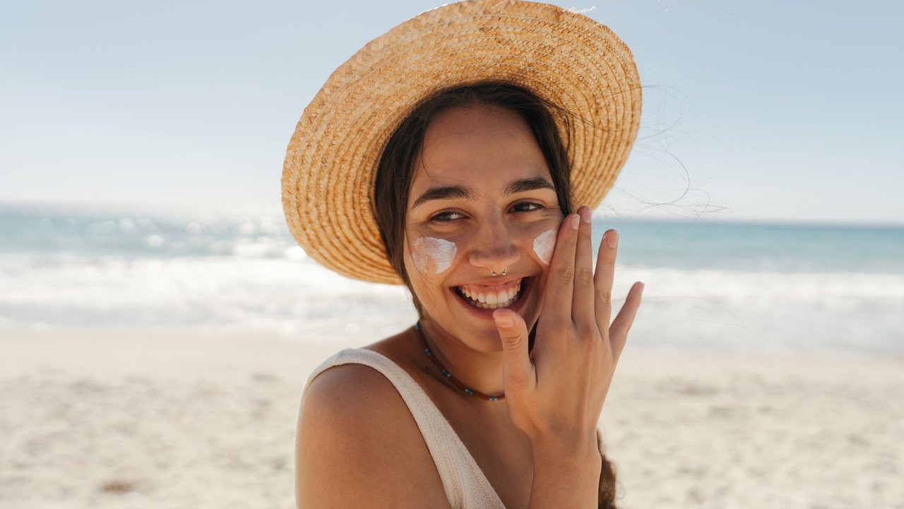 Photo of a young woman applying sunscreen on her face while at the beach