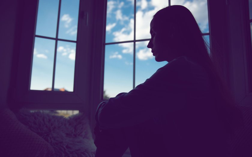 Bedrückte Frau sitzt drinnen, während draußen die Sonne scheint