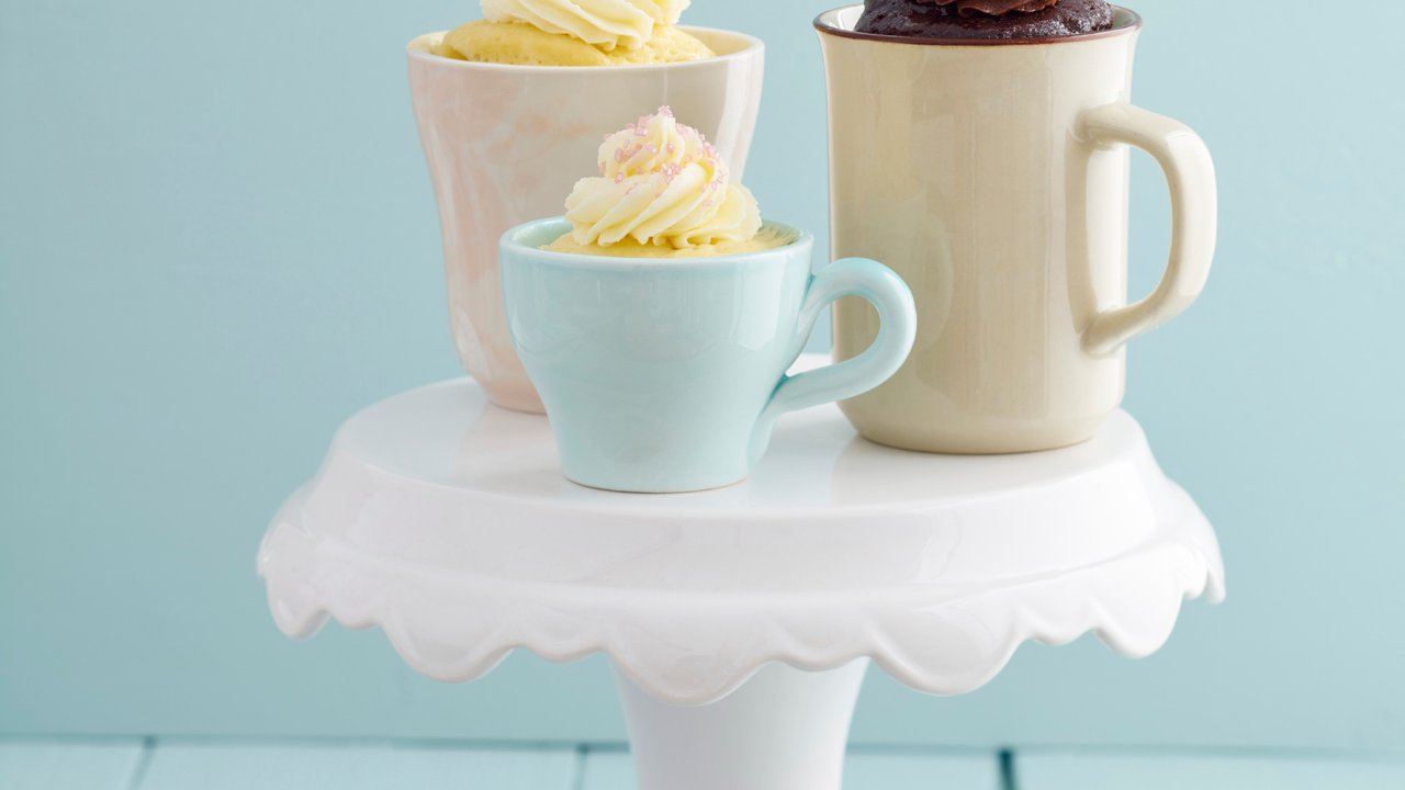 Vanilla and chocolate mug cakes with frosting  and raspberries on a cake stand