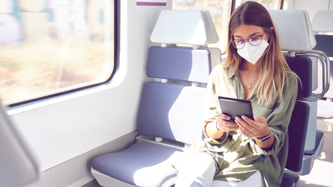 Young woman wearing face mask and reading a e-book in the train. New normal travel concept.