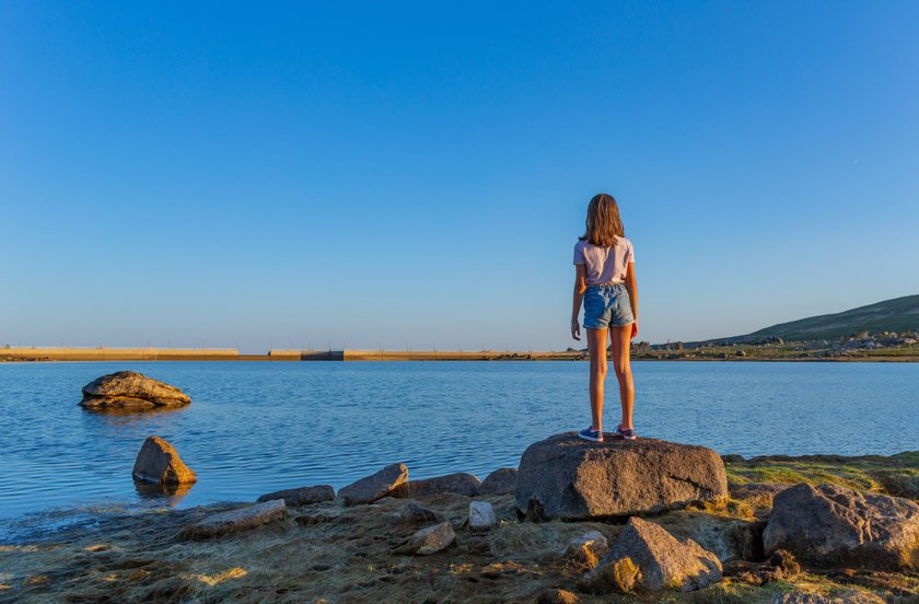 Eine Frau steht am Wasser auf Felsen vor blauem Himmel