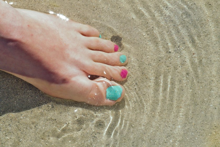 Frau hält Fuß mit lackierten Nägeln ins Wasser