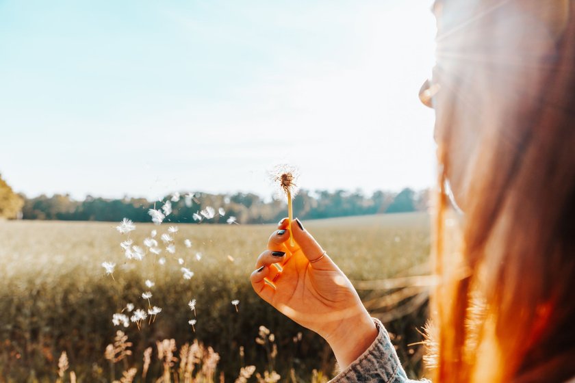 Junge Frau bläst Pusteblume und wünscht sich etwas.